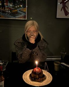 a woman sitting in front of a cake with a lit candle on top of it