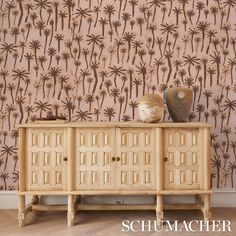 a sideboard in front of a wall with palm trees on it and a vase next to it