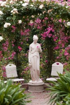 there is a statue in the middle of some flowers and two benches near one another