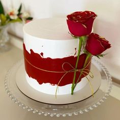 there is a white cake with red icing and two roses on the top one