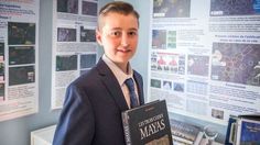 a young man in a suit and tie holding up a book next to a poster