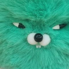 a green stuffed animal with black eyes and white nose is shown in close up view