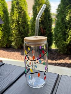 a glass cup with a straw in it sitting on a wooden table next to some bushes