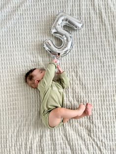 a baby laying on top of a bed next to a number balloon