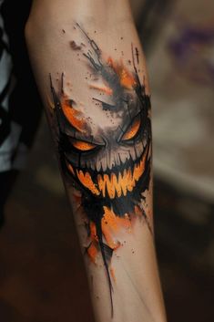 a tattoo with an orange and black design on it's arm that has a scary face