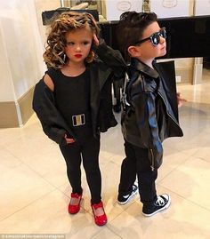 two young children standing next to each other wearing black clothing and red shoes, one with sunglasses on his head