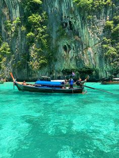 two people in a boat on the clear blue water near some cliffs and green trees