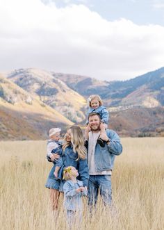 a man, woman and two children standing in tall grass with mountains in the background