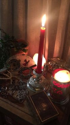 a lit candle sitting on top of a wooden table next to jewelry and a potted plant