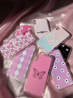 four cases with butterflies and hearts on them are laying on a pink satin surface,