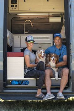 a man and woman sitting in the back of a van with two dogs