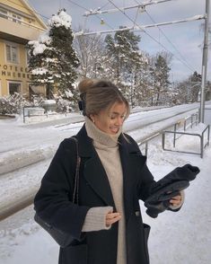 a woman is standing in the snow with her coat open and looking at something on her hand