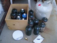 an assortment of propane gas bottles sitting on the ground next to a box with lids