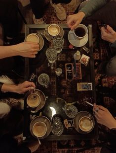 four people sitting at a table with cups of coffee in front of them and one person holding a spoon