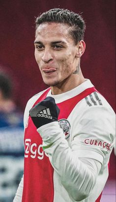 a soccer player with his hand up in the air while wearing a red and white uniform