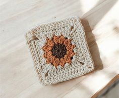 a crocheted square with an orange and brown flower on it sitting on top of a wooden table