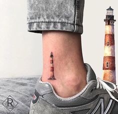 a foot with a small lighthouse tattoo on it's side next to a light house