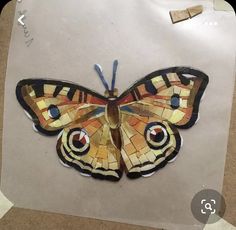 a butterfly made out of stained glass sitting on top of a piece of paper