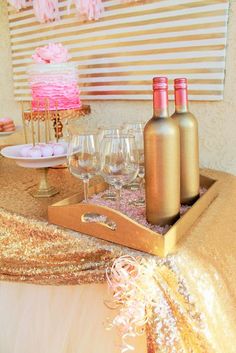 a table topped with wine glasses next to a pink and gold cake covered in confetti