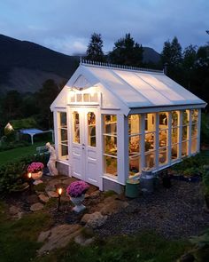 a small white house with lights on it's windows in the grass and flowers