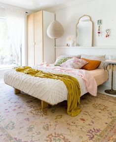 a bedroom with a bed, mirror and rug on the floor in front of it