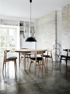 a dining room table and chairs in front of a brick wall with an open window