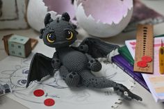 a crocheted dragon sitting on top of a table next to markers and pencils