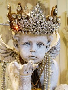 a white statue wearing a crown with pearls on it's head and hands in the air