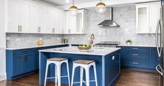 two stools sit at the center of this kitchen island with marble countertops and blue cabinets