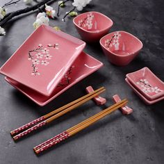 pink dishes and chopsticks with cherry blossoms on them, along with two wooden chopsticks