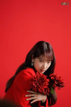 a woman with long dark hair wearing a red dress and holding flowers in her hands