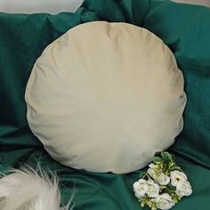 a round pillow sitting on top of a green blanket next to white flowers and feathers