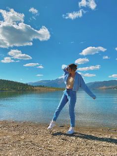 a man standing on the shore of a lake with his arms in the air while wearing blue sweatpants