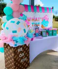 an ice cream stand with balloons and other items on the table in front of it that says, what's the he or she?