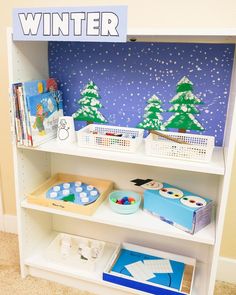 a white book shelf filled with books and other items next to a blue winter wallpaper