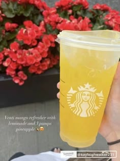 a person holding up a plastic cup with a starbucks logo on it and flowers in the background