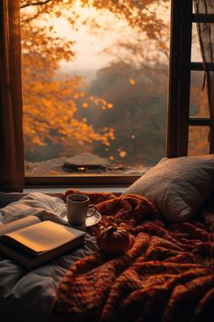 a cup of coffee and an open book on a bed in front of a window