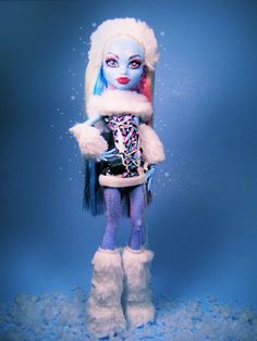 there is a doll with blue hair and white fur on it's head, standing in the snow