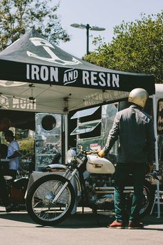 a man standing next to a motorcycle under a tent with iron and resinin written on it