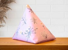 a pink triangle shaped pillow sitting on top of a wooden table next to a potted plant