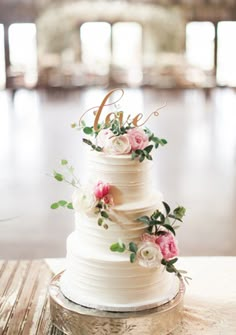 a white wedding cake with pink flowers and the word love on top is sitting on a table