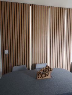 a wooden sign sitting on top of a table next to a wall with vertical blinds