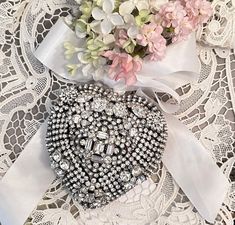 a heart shaped brooch sitting on top of a lace doily next to flowers