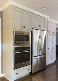 a stainless steel refrigerator and oven in a kitchen with white cabinets, wood floors and hard wood flooring