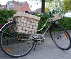 a bicycle with two baskets on the front is parked next to some bushes and shrubbery