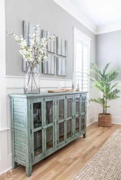 a vase with flowers sitting on top of a wooden cabinet next to a plant in a vase