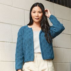 a woman standing in front of a brick wall wearing a blue cardigan and tan pants