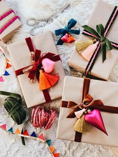 four wrapped presents with tassels and bows on them sitting on a white blanket