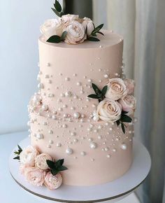 a three tiered wedding cake with pink flowers and pearls on the top, sitting on a table