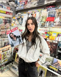 a woman holding up a magazine in front of a wall full of magazines and magazines